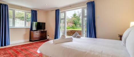 A hotel room with a large bed, a TV, and a view of the garden through the windows.