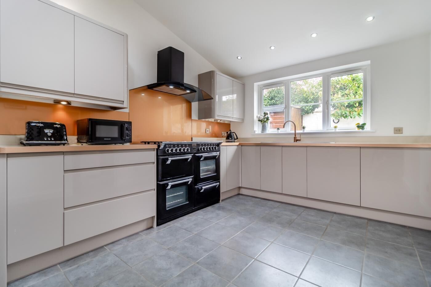 A modern kitchen with built-in appliances, a large window, and a view of greenery outside.