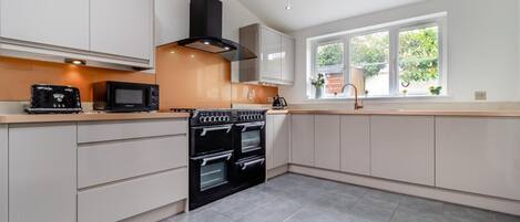 A modern kitchen with built-in appliances, a large window, and a view of greenery outside.