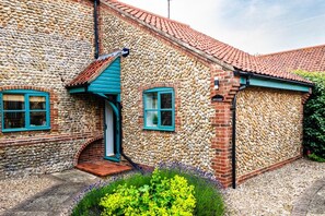 A stone building with a blue door and windows, a red roof, and a sign reading "Grove Barn". - 2 Bed in Langham (oc-g25208) (Langham)