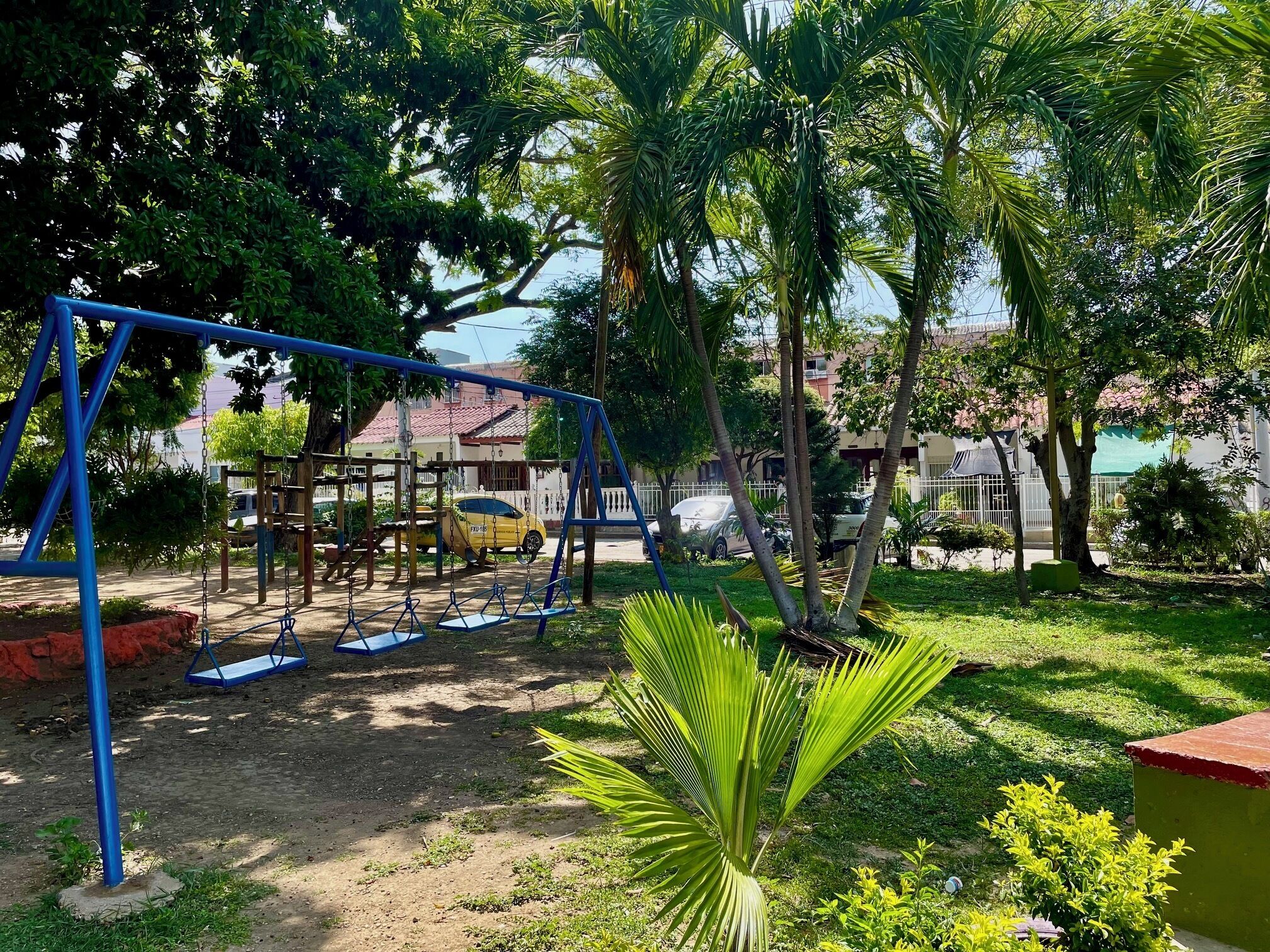 A playground with swings and a slide, surrounded by trees and a building in the background.