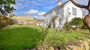 A white house with a well-maintained lawn and a stone structure in the background. - 2 Bed in Pencaenewydd (oc-t29187) (Pencaenewydd)
