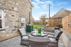 Un patio exterior con mobiliario de mimbre, un armario verde y una parrilla de barbacoa.