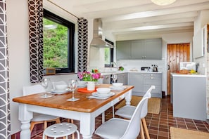 A modern kitchen with grey cabinets, a wooden dining table, and a view of greenery outside. - 2 Bed in Aberdaron (oc-y29261) (Aberdaron)