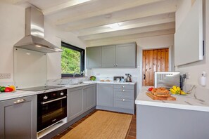 Uma cozinha moderna com armários cinzas, forno embutido e janela com vista para o verde.