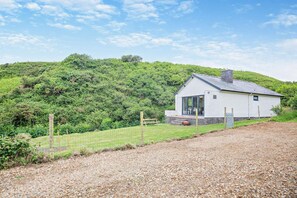 A white house with a sloped roof, surrounded by a gravel driveway and a wire fence. - 2 Bed in Aberdaron (oc-y29261) (Aberdaron)