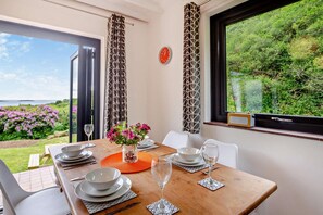 A dining area with a table set for two, a vase with flowers, and a view of the outdoors. - 2 Bed in Aberdaron (oc-y29261) (Aberdaron)