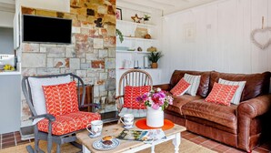 Ein gemütliches Wohnzimmer mit einer Steinwand, einem braunen Ledersofa und einem Schaukelstuhl mit roten Kissen.