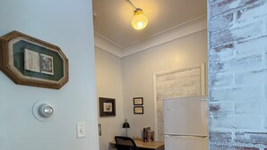 A compact kitchen with a wooden countertop, a black office chair, a white refrigerator, and a wall-mounted light fixture.