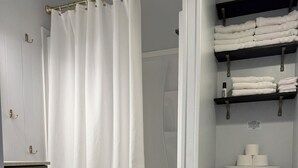 A bathroom with a shower, toilet, and a shelf with folded towels.