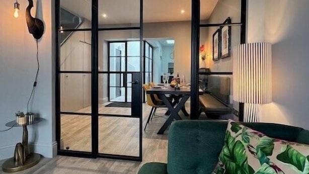 A modern living room with a green sofa, a dining area with a table and chairs, and a kitchen in the background. - 3 Bed in Fowey (oc-p29280) (Fowey)