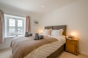 Ein Schlafzimmer mit einem Bett, einem Nachttisch mit Lampe und einem Fenster mit Vorhängen.