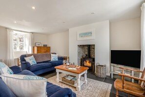 Ein Wohnzimmer mit einer Couch, einem Couchtisch, einem Kamin, einem Fernseher und einem Fenster.