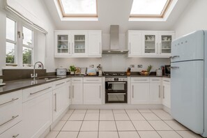 Une cuisine moderne avec des meubles blancs, un four encastré, une cuisinière à gaz et un réfrigérateur blanc.
