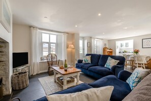 Ein Wohnzimmer mit blauem Sofa, Holztisch, Fernseher und Kamin.