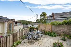 A patio with a table set for dining, surrounded by a wooden fence and various plants. - 3 Bed in Golant (oc-o29307) (Golant)