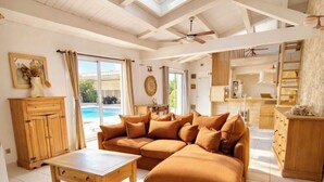 A spacious living room with a large sectional sofa, a wooden coffee table, and a view of a swimming pool through large windows. - Charming house with pool, 10 min from La Rochelle (Dompierre-sur-Mer)