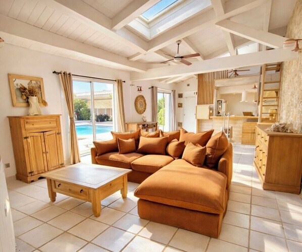 A spacious living room with a large sectional sofa, a wooden coffee table, and a view of a swimming pool through large windows. - Charming house with pool, 10 min from La Rochelle (Dompierre-sur-Mer)