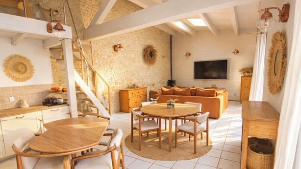 A spacious living area with a round wooden table and chairs, a sofa, and a television. - Charming house with pool, 10 min from La Rochelle (Dompierre-sur-Mer)