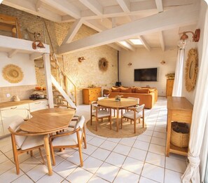 Uma sala de estar ampla com uma mesa de madeira redonda e cadeiras, um sofá e uma televisão.
