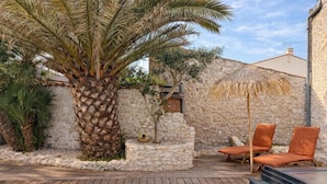 A swimming pool with a wooden deck, a palm tree, and a stone wall. - Charming house with pool, 10 min from La Rochelle (Dompierre-sur-Mer)