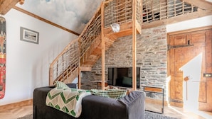 Una habitación acogedora con chimenea de piedra, una escalera de madera y un sofá cómodo.