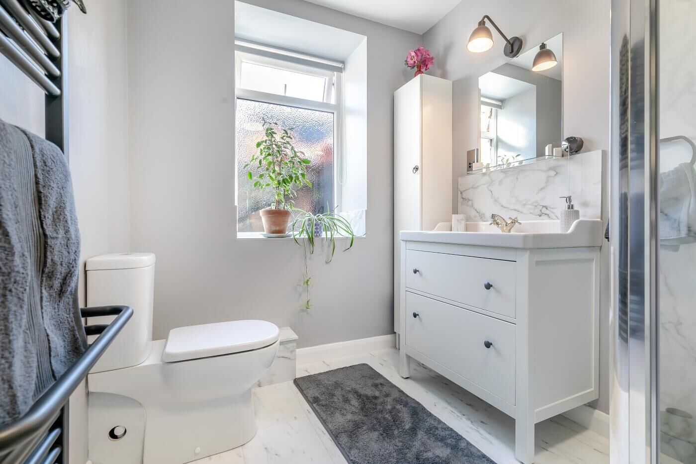 Een moderne badkamer met toilet, wastafel en douche. Er is een raam met een plant en een spiegel boven de wastafel.