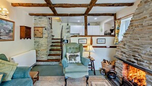 Una sala de estar acogedora con chimenea de piedra, un sillón verde y una escalera que lleva a una zona de cocina.