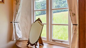Una habitación con un ventanal grande, una silla de madera y un espejo sobre un pedestal.