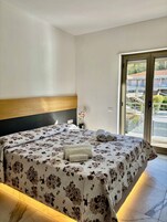 Una cama bien hecha con una colcha floral, un cabecero de madera y vistas a un balcón con barandilla y vegetación.