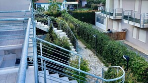 Zona residencial amb una escala que mena a un balcó, envoltada de verdura i cases.