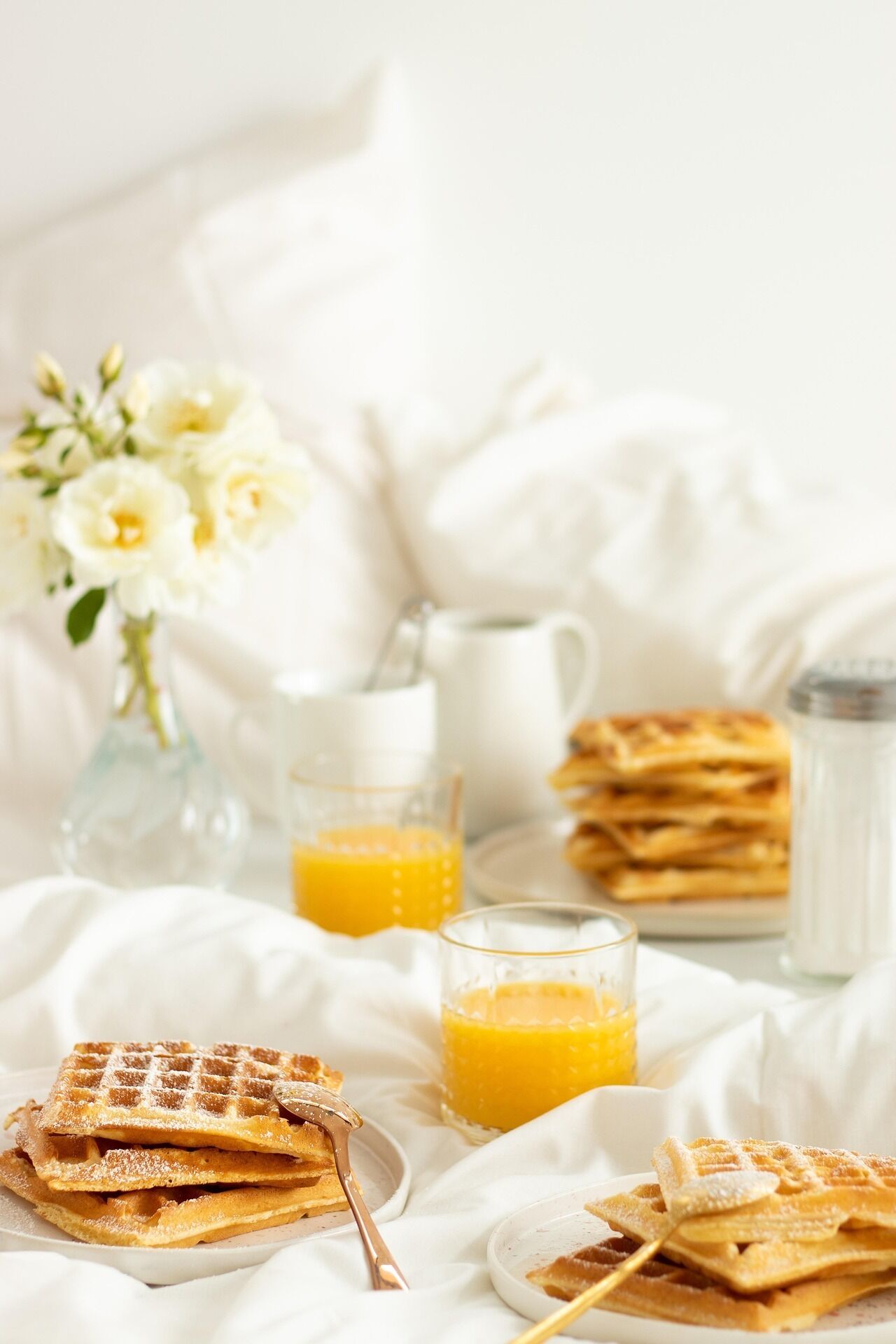 A breakfast setting with waffles, orange juice, and a vase of flowers.