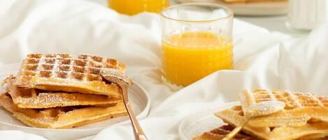 Un desayuno con waffles, jugo de naranja y un florero de flores.