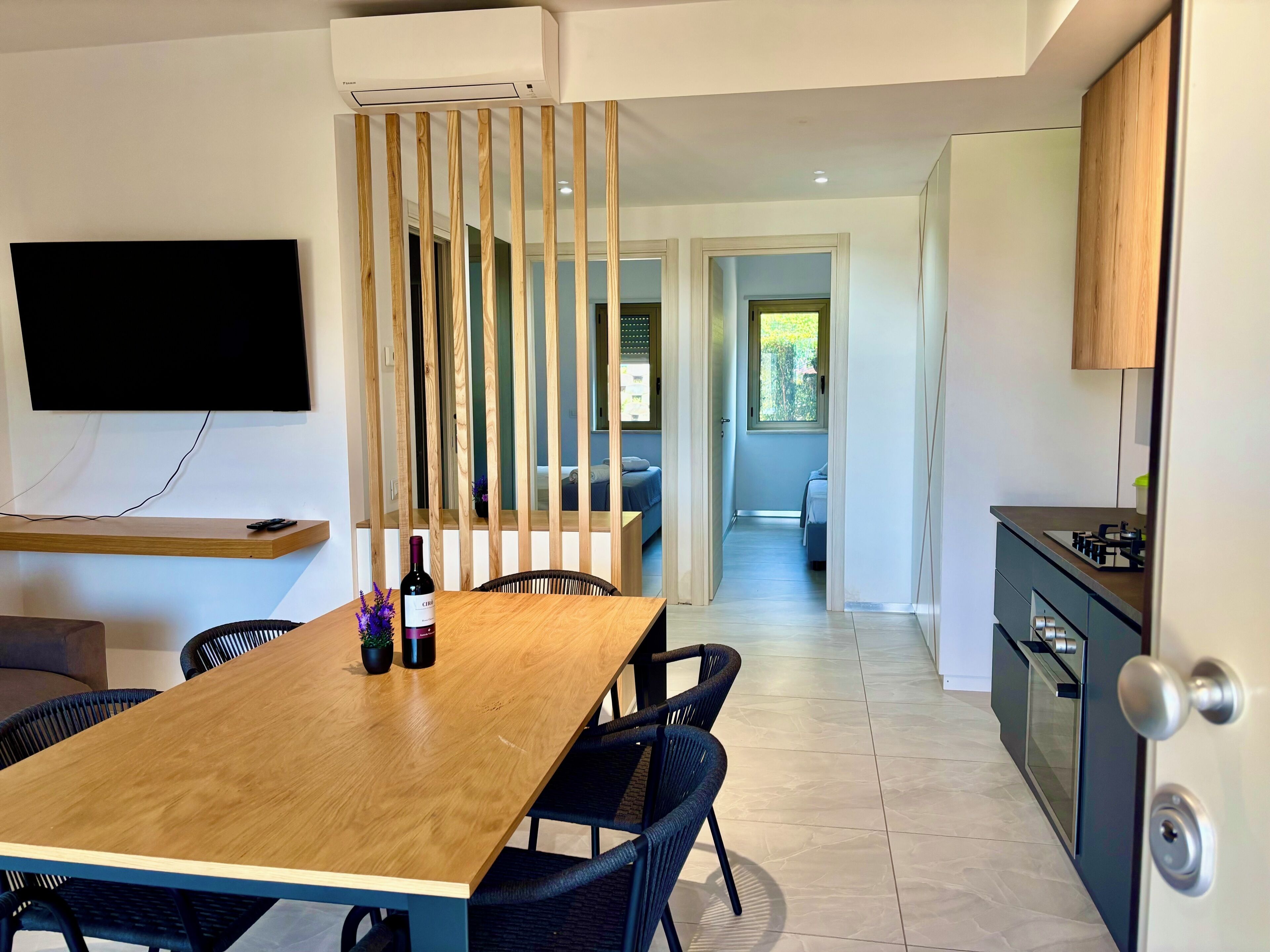 A modern kitchen with a wooden dining table, chairs, and a TV mounted on the wall.