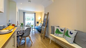 A compact living space with a kitchenette, dining area, and a sofa with bird-themed cushions. - 2 Bed in Rye (oc-52470) (Rye)