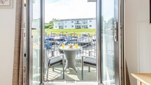 A balcony with a table and chairs, a view of parked vehicles, and a building in the background. - 4 Bed in Abersoch (oc-b29438) (Abersoch)