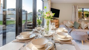 Ein Essbereich mit Tisch für vier Personen, einem Blumenstrauß in einer Vase und einer Couch im Hintergrund.