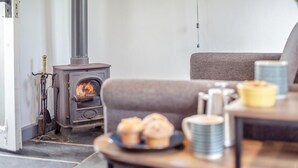 Un salon chaleureux avec un poêle à bois, un canapé et une table où sont disposés des produits de boulangerie.