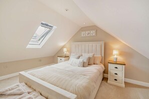 A bedroom with a sloped ceiling, a skylight, a bed with white bedding, two bedside tables with lamps, and a small wall-mounted shelf. - 1 Bed in Llanteg (oc-b29484) (Llanteg)
