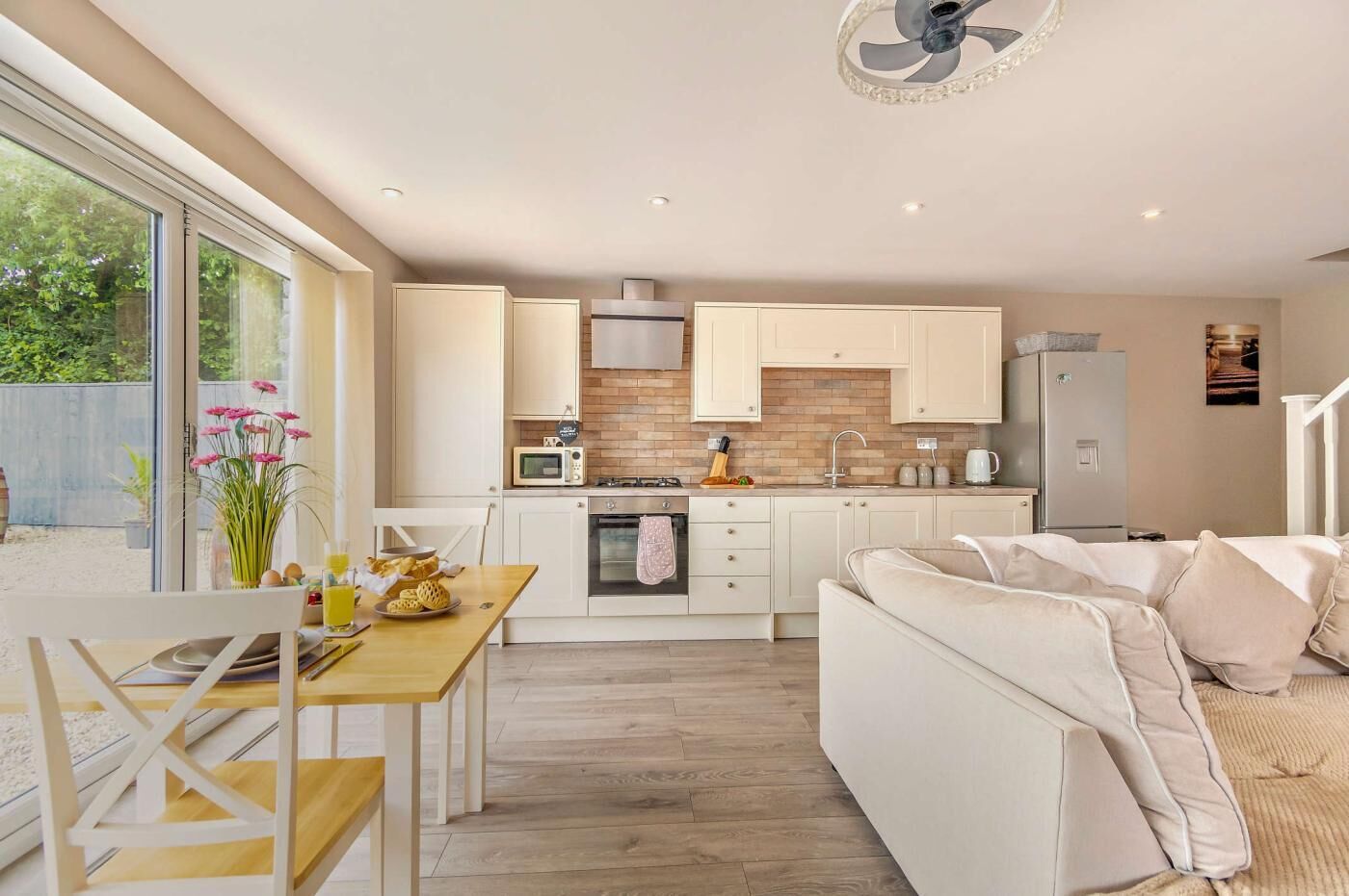 A modern kitchen with white cabinets, a microwave, and a refrigerator. There is a dining area with a table and chairs, and a sofa in the living room.
