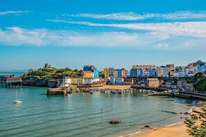 Une ville côtière aux bâtiments aux couleurs vives, un port où sont amarrés des bateaux et un phare perché sur une colline.