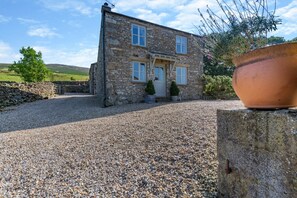 A stone house with a gravel driveway and a large terracotta pot in the foreground. - 2 Bed in Middleton (oc-m29515) (Middleton)