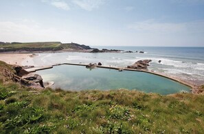 Paisagem costeira com piscina cristalina, praia arenosa e afloramentos rochosos.