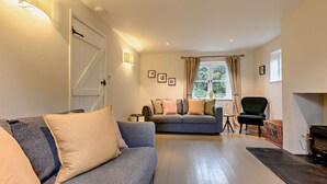 Ein Wohnzimmer mit einer Couch, einem Sessel, einem Kamin und einem fenster mit Vorhängen.