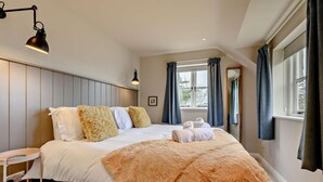Ein Schlafzimmer mit einem Bett, Kissen, einer flauschigen Decke, einem Nachttisch, einer Lampe und einem Fenster mit Vorhängen.
