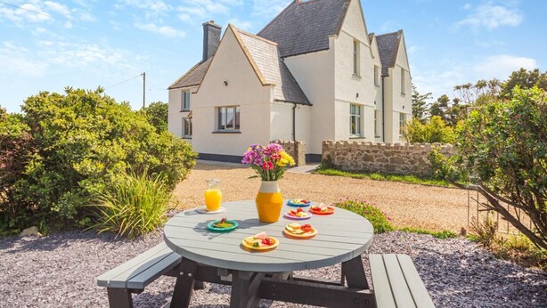 Ein Haus mit Garten, einer Patio-Sitzgruppe gedeckt mit Speisen und Getränken, umgeben von viel Grün.