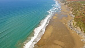 An aerial view of a coastal landscape with a sandy beach, a clear blue ocean, and distant hills. - 3 Bed in Looe (oc-j29456) (Looe)