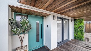 A modern house with a teal door, a wooden deck, and a green vertical garden. - 3 Bed in Looe (oc-j29456) (Looe)