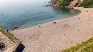 Ein Strand mit klarem Wasser, einer Steinmauer und einer grasbewachsenen Klippe.