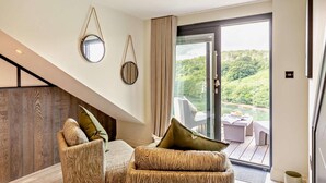 Ein modernes Wohnzimmer mit Treppe, zwei Sesseln, einer Couch und einem großen Schiebeglastür, die auf einen Balkon mit schöner Aussicht führt.